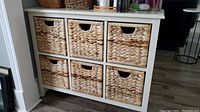 Front view of a white wooden storage shelf with six woven baskets arranged in two rows of three.
