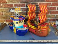 Photo of two Fisher Price toy pirate ships with one larger brown ship with red and yellow sails and one smaller blue and yellow ship