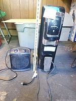 Photo of two black space heaters side by side showing size difference and design, wooden panel background