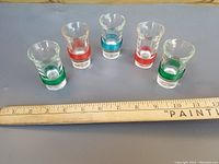 Photo of 5 glass shot glasses with colored bands and a ruler for size reference.