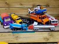 Photo showing eight large toy vehicles including various trucks and a helicopter on a wooden background, highlighting the lot contents
