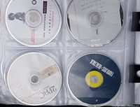 Close-up photo of four music CDs in clear plastic sleeves inside the binder, showing artists The Notorious B.I.G., 2Pac, Koolos, and one more.