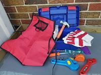 Blue and red child's tool box with various plastic toy tools, a red apron, gloves, and safety glasses arranged outside the box
