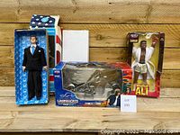 Front view of the three boxed collectible figures: JFK talking figure, American Chopper Jet Bike, and Muhammad Ali figure.