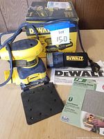 DeWalt sander kit showing sander, cloth dust bag with DeWalt logo, sandpaper punch plate, 80 grit finishing sandpaper, and original box.