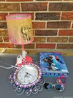 Frozen themed lamp with pink trimmed character shade, jeweled wall clock, and Frozen activity set on wooden surface against brick wall