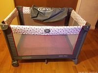 Gray and rose motif Graco Pack 'n Play playard on hardwood floor with carry bag inside