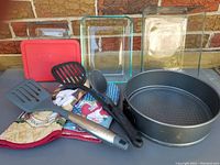 Image showing glass dishes (Pyrex 3 cup with lid, Pyrex 6 cup, Anchor 11 cup), 9-inch springform pan, two fabric oven mitts, and three cooking utensils (two spatulas, one ladle) arranged outdoors against a brick wall.