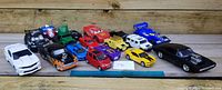 Front row of 14 die-cast toy vehicles including various car models in different colors and styles on wooden background
