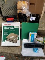 Photo of 20 recycled green hanging folders with tabs, boxes of staples, staplers, envelopes, index cards, and black hole puncher arranged on a surface