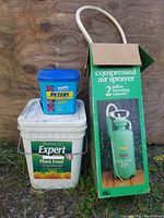 2 Gallon Compressed Air Sprayer in original box, Schultz Expert All Purpose Plant Food 25 lb bucket, and blue container of Peter's Azalea Food placed together on outdoor wood surface.