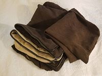Four folded faux suede throw pillow covers in tan and different shades of brown, stacked to show faux leather piping on some and nylon/plastic zippers on others.