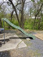 Full side view of green wave slide set up outdoors, showing its length, wavy shape, and metal support frame at top.