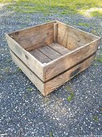 Rustic wooden box with visible weathering and steel strap around the sides, open top, placed on gravel ground outside.