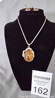 Photo shows an amber pendant necklace on a black display bust with a twisted silver-tone chain and a large water drop-shaped amber stone in an ornamental silver-tone setting.