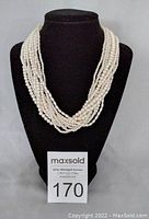 Full view of 10 strand white faux pearl necklace displayed on black stand.