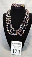 Three strands multicoloured glass beads necklace displayed on black jewelry stand