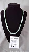 Full view of green jade beaded necklace displayed on black jewelry bust with MaxSold auction number 172 in front.