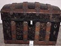 Front and top angle showing wood strips, leather straps, ornate metal decorations, and domed top on the trunk.
