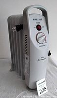 Side angled view of the white Airworks mini oil heater showing power switch and thermostat dial with handle on top and power cord.