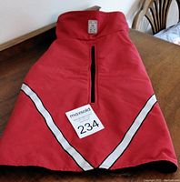 Red dog coat laid flat on wooden surface showing front zipper and glow in the dark reflective stripes.