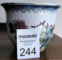 Front view of the flower pot showing floral blossom, bird design, and gold gilt raised details with auction lot number card in front.