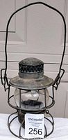Front view of the antique oil lantern with wire handle and round glass globe, metal frame and base visible