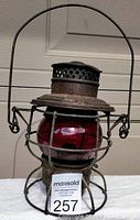 Front view of antique red globe lantern with protective metal cage, showing patina and details of the globe and burner.