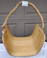 Front view of curved wood firewood basket with thick rope handle hanging above, measured for size.