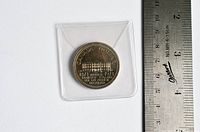 Photo of the coin's reverse side showing the PEI building and commemorative text with a measuring ruler beside it.
