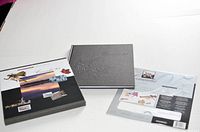Two stamp book covers shown: one black embossed with maple leaf, the other with a Canadian-themed printed jacket featuring scenic photos and stamp images