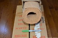Single cork roll partially out of box showing rolled cork material and scale marker (sharpie)