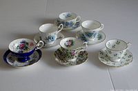 Front view showing all six floral teacups and saucers arranged in two rows on a light surface