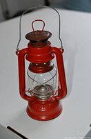 Red metal vintage oil lamp with glass globe and handle on white surface