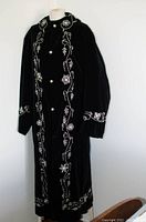 Full view of the black velvet conductor's overcoat showing its length, embroidery along front edges and sleeves, and overall condition.