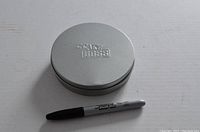 Round silver metal tin with embossed 'Cake Boss' logo on lid next to a Sharpie pen for scale.