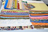 Wide view of folded fat quarter quilting fabric, showing variety of colors and patterns including stripes, florals, and novelty prints.