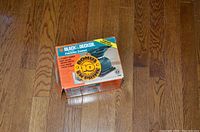 Box of Black & Decker finishing sander on wooden floor, orange and black graphics with product info visible