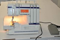 Front view of Husqvarna Viking Huskylock 936 serger machine powered on with LED work light illuminated; foot pedal visible