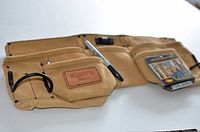 Full view of tan leather carpenter apron showing multiple pockets, stitched reinforcements, and pen loop.