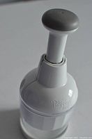 Side view of Pampered Chef chopper showing white upper body and grey plunger top with brand logo visible.