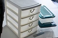 Four-drawer plastic storage unit with translucent drawers and beige frame alongside two clear lidded plastic containers, with a ruler for scale.