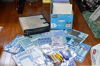 Photo showing pre-made scrapbook pages, crafting kits, a carrying case, and cutting tools laid on a wooden floor.