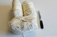 Three skeins of cream/light tan yarn with labels visible, placed next to a black marker for scale.