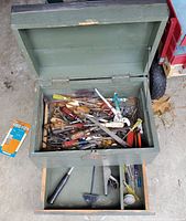 Photo of open antique green wooden tool chest showing top compartment filled with various screwdrivers, pliers, files, and other small hand tools.