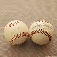 Two autographed baseballs signed by Jim Rice and Tim Wakefield placed side by side on a striped fabric.
