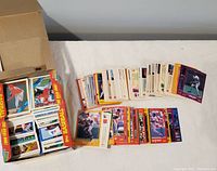 Box with many 1980s baseball cards stacked loosely, some laid out for display showing colorful vintage cards with players.