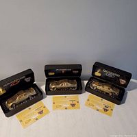 Three gold edition NASCAR diecast cars in black display cases with certificates of authenticity laid in front on a white surface.