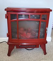 Red freestanding electric fireplace with glass door showing faux logs inside, standing on carpeted floor