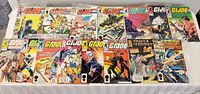 Top view of 18 GI Joe and Transformers comic books, laid out on a white table showing covers with colorful artwork and characters, mostly with comic text and Marvel branding.